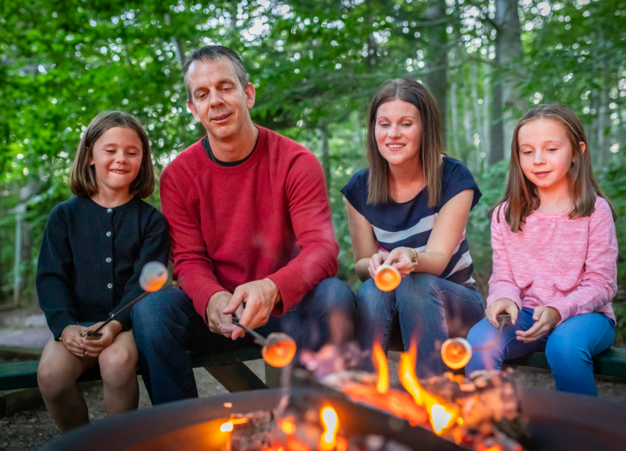 A family sitting at a campsite roasting marshmallows over a fire. 