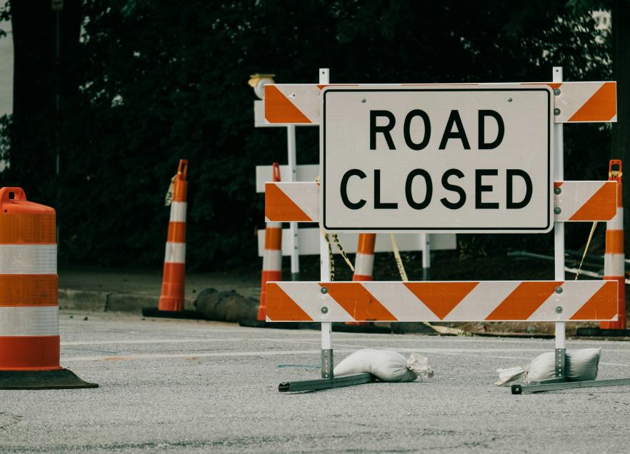 A road closed sign with pylons around it. 