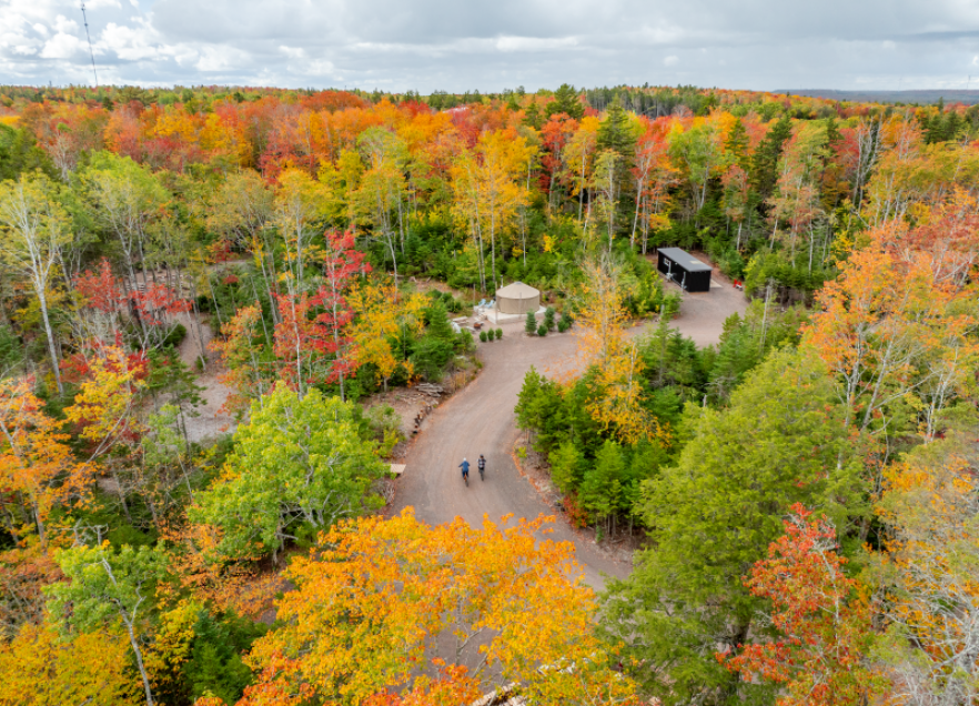 A drone view of a forest in the fall. There is a yurt accommodation in the view among leaves that have changed colours in the fall. Drone view of accommodations - Location: Seek Wilderness Accommodation, Truro, Bay of Fundy & Annapolis Valley 