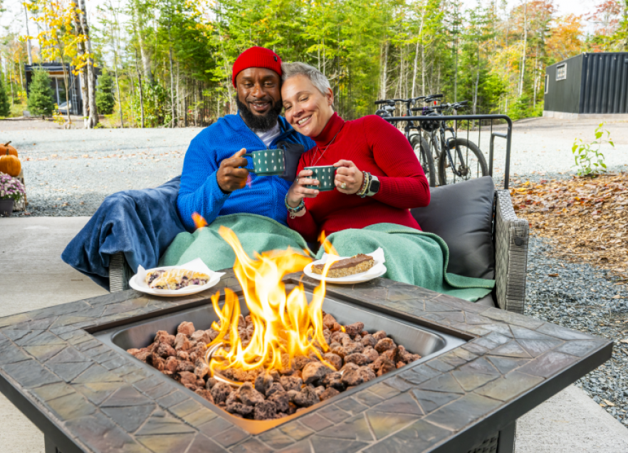 Two people sitting cuddling next to an outdoor fire table.
