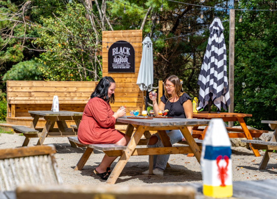 Black Harbour Distillers in Hubbards. Two people are sitting at a picnic table enjoying a meal. 