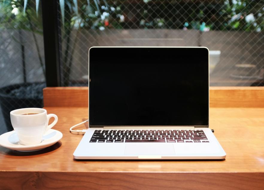 A laptop is open on a countertop. There is a coffee cup next to the computer. 
