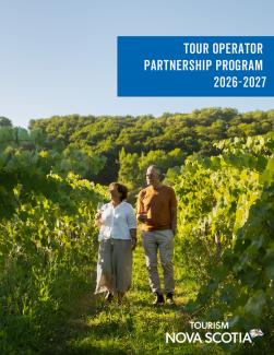 Two people walking in a green vineyard holding a glass of wine